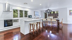 A modern kitchen with white cabinetry, a central island with bar stools, and a dining area with a large window overlooking greenery.