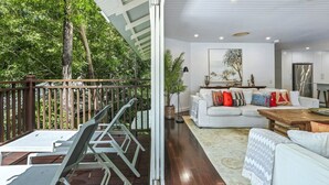 A modern living room with a white sofa, a wooden dining table, and a balcony with metal chairs.