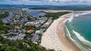 An aerial view of a coastal area with a beach, a marina, and a residential area with houses and buildings.