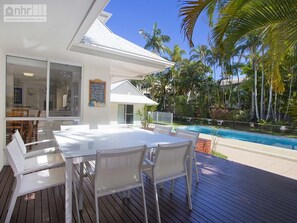 Un área de comedor al aire libre moderna con piscina y palmeras.