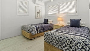 Une chambre avec deux lits, des murs blancs et un ventilateur de plafond.
