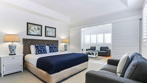 A modern bedroom with a large bed, two bedside tables, a gray sofa, and a small table with chairs. - Island living in the heart of Noosa (Noosa Heads)