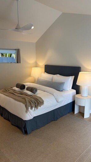 A modern bedroom with a large bed, two bedside lamps, and a ceiling fan.