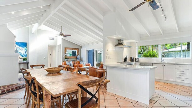 A spacious dining area with a wooden table and chairs, a kitchen with white cabinets, and a ceiling fan. - Island living in the heart of Noosa (Noosa Heads)
