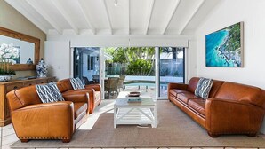 A living room with leather sofas, a coffee table, and a large glass door leading to a pool area. - Island living in the heart of Noosa (Noosa Heads)