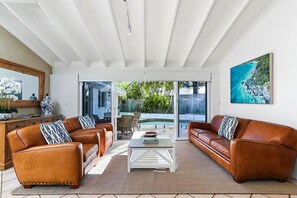 Relax in a spacious living room with a glass door leading to an outdoor area, a large painting, and comfortable leather sofas.
