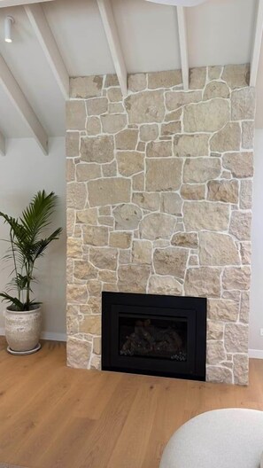 A stone fireplace with a black surround, a potted plant to the left, and wooden flooring. - Island living in the heart of Noosa (Noosa Heads)