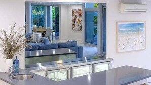 A modern kitchen with a bar area, a dining area with a blue sofa, and a view of greenery outside. - 31 Witta Circle, Noosa Heads (Noosa Heads)