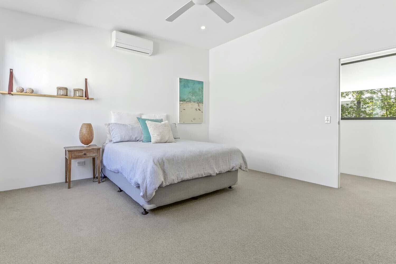 A bedroom with a bed, a bedside table, a wall-mounted air conditioner, and a shelf with decorative items.