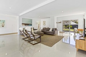 Relax in this open-plan living space with a high ceiling, comfortable seating area, and large window offering a view of the outdoors.