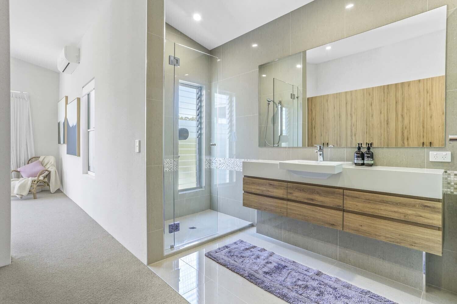 A modern bathroom with a glass-enclosed shower, a large mirror, and a wooden vanity.
