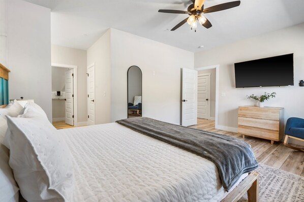 Un dormitorio con cama, ventilador de techo, televisor, cómoda y espejo.
