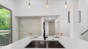 A modern kitchen with a central island, a stainless steel sink, and pendant lighting.