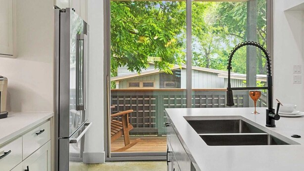 A modern kitchen with a large sliding glass door leading to a deck, a built-in sink, and a refrigerator.