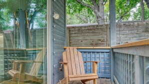 A wooden rocking chair on a wooden deck with a glass door and a blue fence.