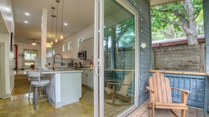 A modern kitchen with a central island, bar stools, and a sliding glass door leading to an outdoor deck with a wooden chair.