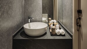 Een moderne badkamer met een groot wit wastafel, donker marmeren wanden en een spiegel die de ruimte weerspiegelt.