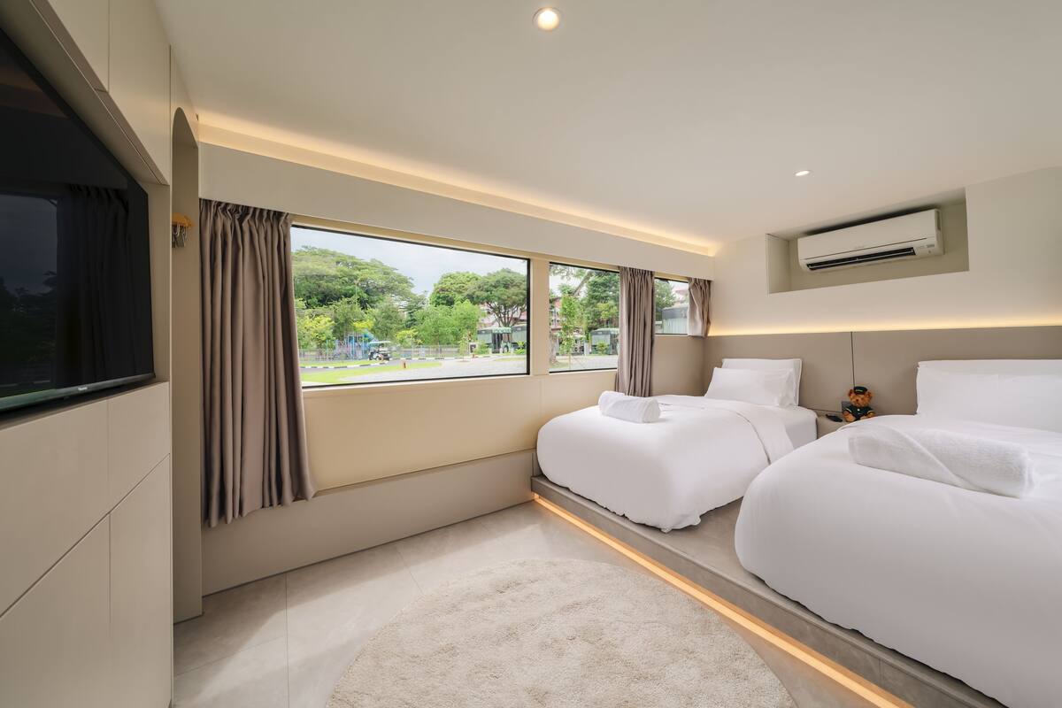 A modern hotel room with two beds, a large window with curtains, an air conditioning unit, and a flat-screen TV.