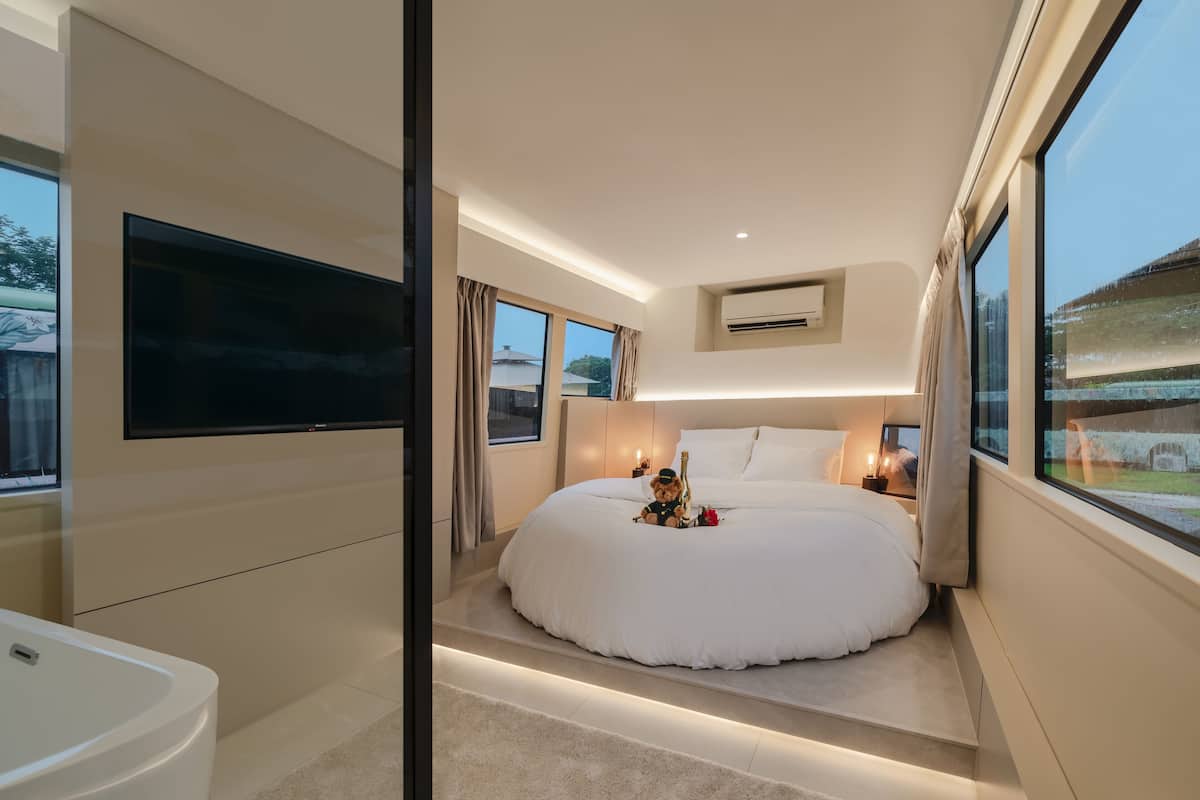 A modern bedroom with a large bed, a TV mounted on the wall, and a window with curtains.