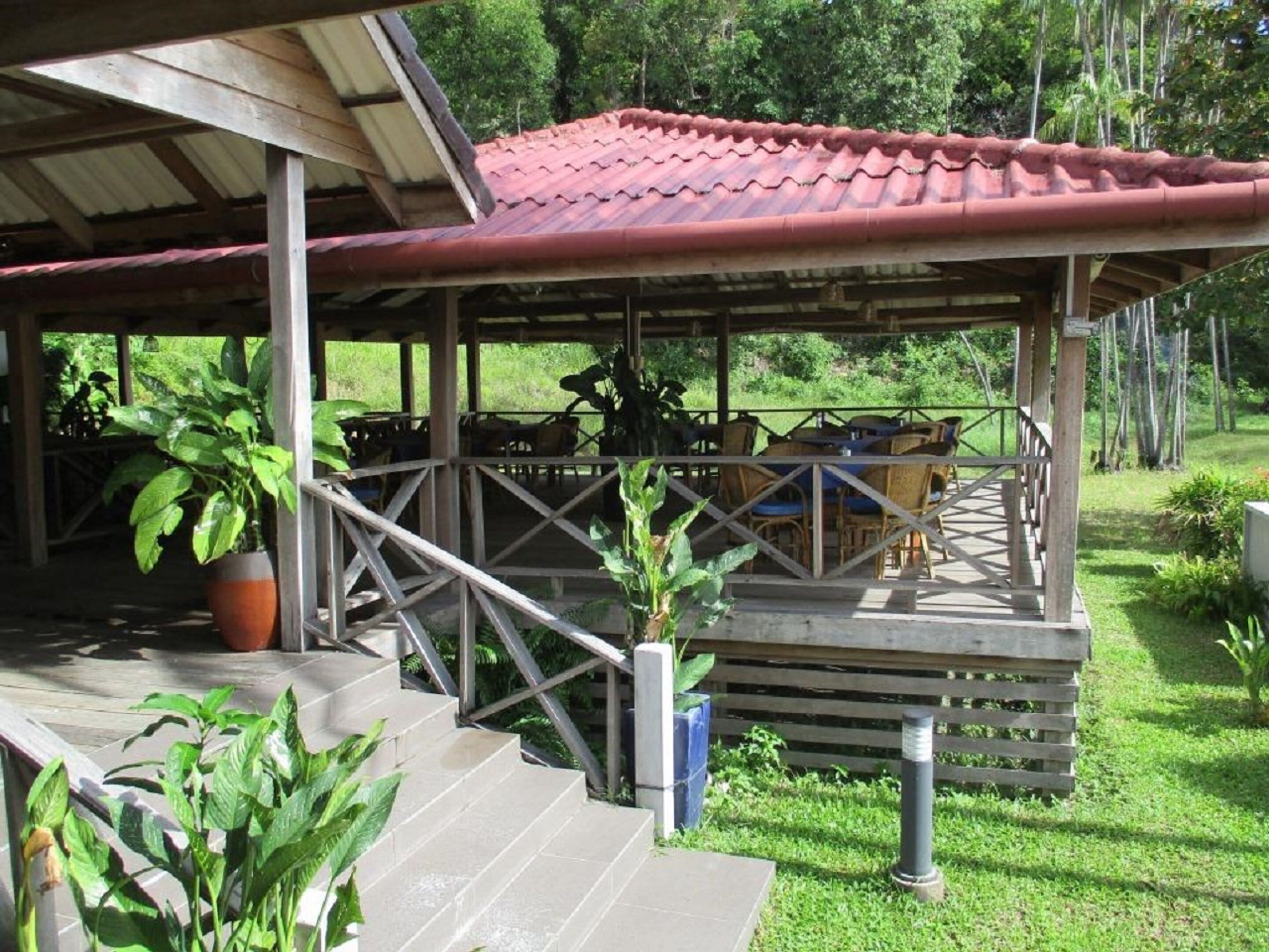 Un espace extérieur abrité, aménagé avec des tables et des chaises, et entouré de verdure.