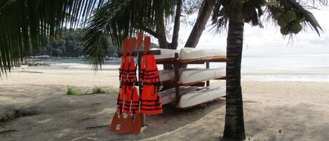 A beach with a stack of white boats and orange life jackets under a palm tree.