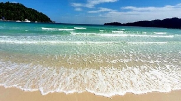 A beach with clear turquoise water, gentle waves, and a distant green hill. - Saracen Bay Resort (Koh Rong Sanloem)