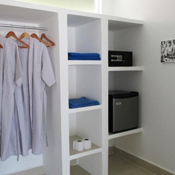 A white wardrobe with hanging robes, a blue towel, a black microwave, and a small refrigerator.