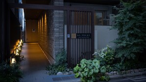 A modern building entrance with a brick facade, a wooden gate, and a pathway lined with plants.