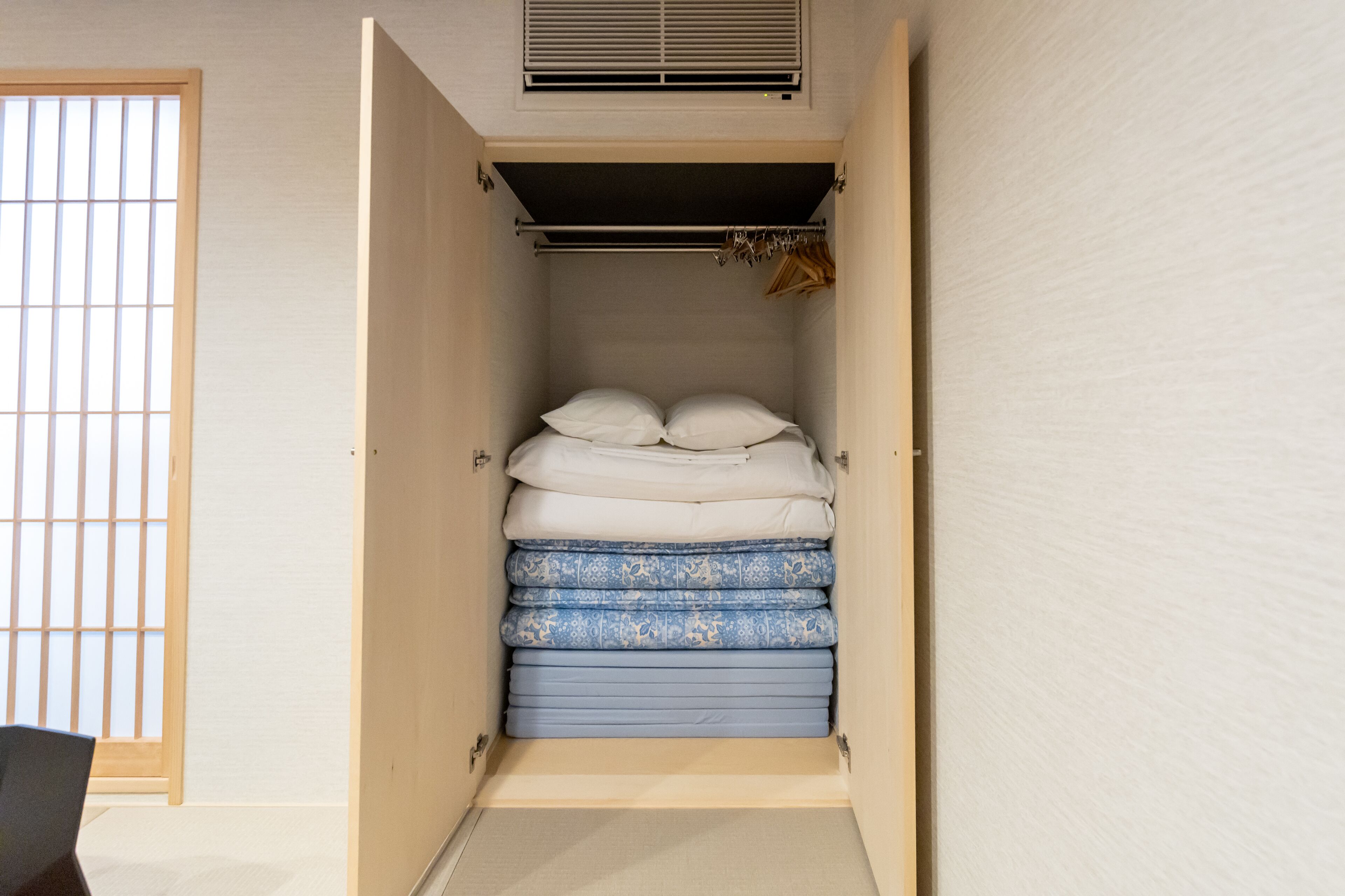 A compact room with a bed, a window with a grid pattern, and a ventilation system above the bed.