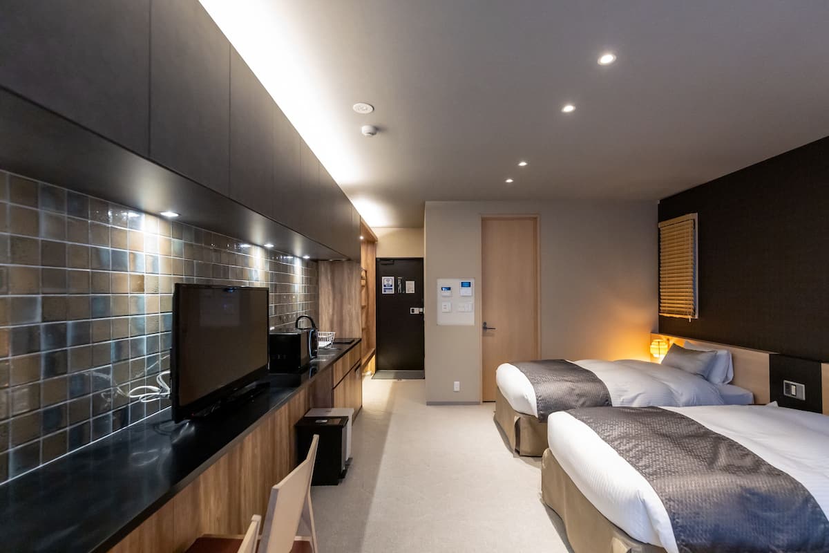 A modern hotel room with a kitchenette, two beds, and a bathroom.