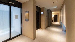 A hotel corridor with a modern design, featuring a flat floor, neutral wall colors, and a television mounted on the wall.