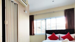 A hotel room with a bed, a window with curtains, an air conditioning unit, and a door with a handle. - KS HOUSE (Bangkok)