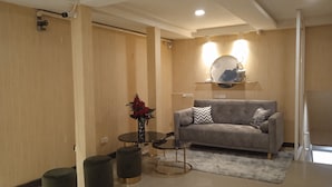 A modern living room with a grey sofa, a round coffee table, and two ottomans. A vase with red flowers is on the coffee table. - KS HOUSE (Bangkok)