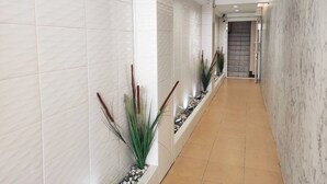 A modern hallway with white tiled walls, a tiled floor, and decorative plants. - KS HOUSE (Bangkok)