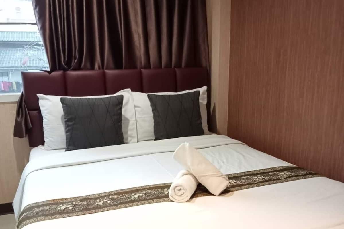A hotel room with a bed, a headboard, and a window with curtains.