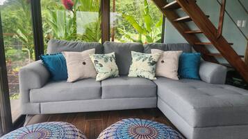 Een grijze modulaire bank met vier kussens, twee ronde poefjes met een blauw-wit patroon, en een houten trap.