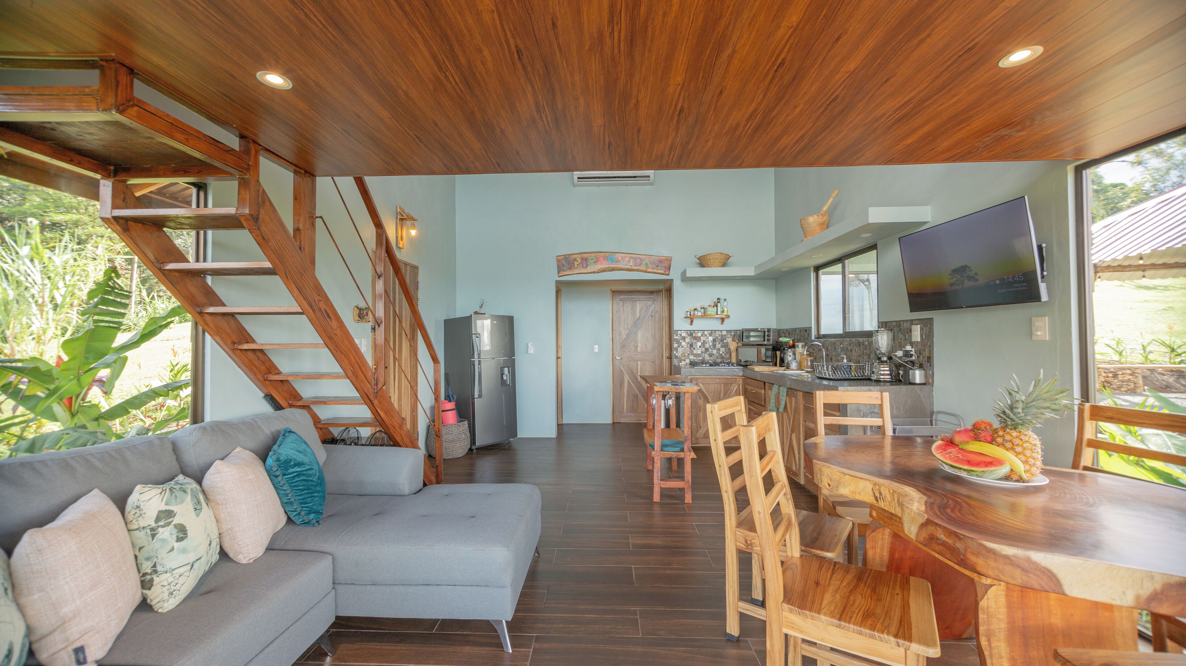 A modern kitchen with wooden accents, a dining area with a wooden table and chairs, and a staircase leading to an upper level.