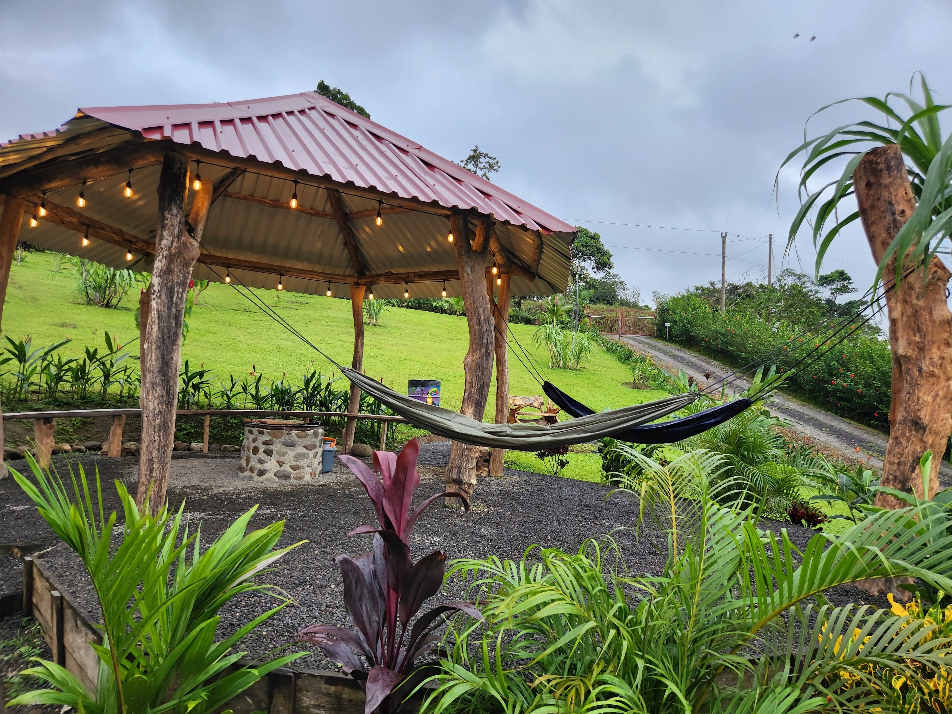 A covered outdoor area with a hammock, a stone planter, and a view of a green landscape.