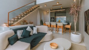 Een moderne woonkamer met een gebogen bank, een salontafel en een trap naar een hoger gelegen verdieping.