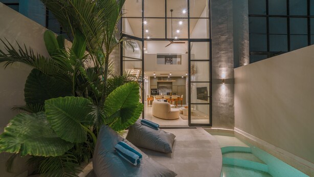 Een modern interieur met een zwembadgedeelte, zitplaatsen en een eethoek, zichtbaar door glazen deuren.
