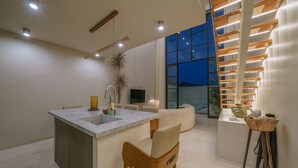 Een moderne keuken met een centraal kookeiland, barstoelen, een spoelbak en een groot raam met uitzicht op een stadsbeeld.