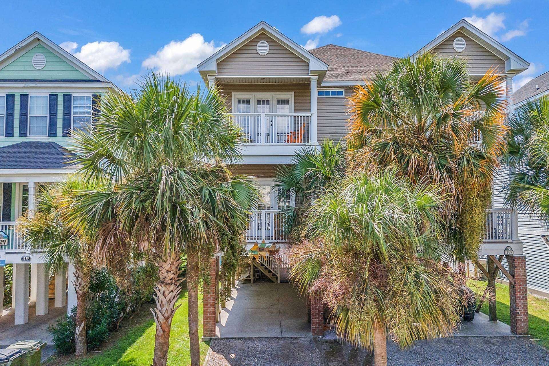 A two-story residential building with a front porch, a staircase leading to the entrance, and a well-maintained lawn with palm trees.