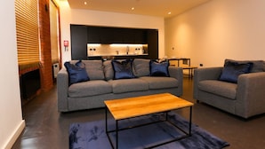 Ein modernes Wohnzimmer mit einer Sofagarnitur, einem Couchtisch und einer Küche im Hintergrund.