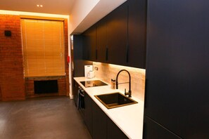 Una cocina moderna con armarios oscuros, una encimera blanca, un lavamanos negro y un horno empotrado.