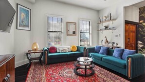 Ein Wohnzimmer mit einem türkisblauen Sofa, einem gemusterten Teppich und einem runden Couchtisch.