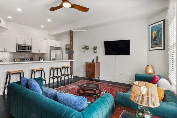 A modern living room with teal sofas, a coffee table, and a TV mounted on the wall.
