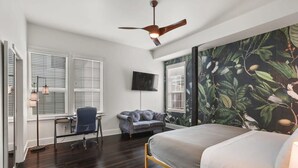 Ein Schlafzimmer mit Bett, Schreibtisch, Stuhl, Sofa, Deckenventilator und Fernseher.