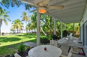 A covered outdoor area with a table and chairs, surrounded by palm trees and a lawn. - Entire Compound on Gated Bayfront Property (Islamorada)