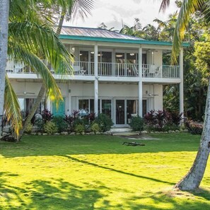 A two-story building with a balcony on the upper floor, surrounded by tropical vegetation. - Entire Compound on Gated Bayfront Property (Islamorada)