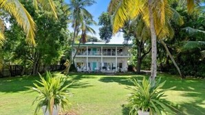 Um edifício de dois andares com varanda, cercado por vegetação exuberante e palmeiras.